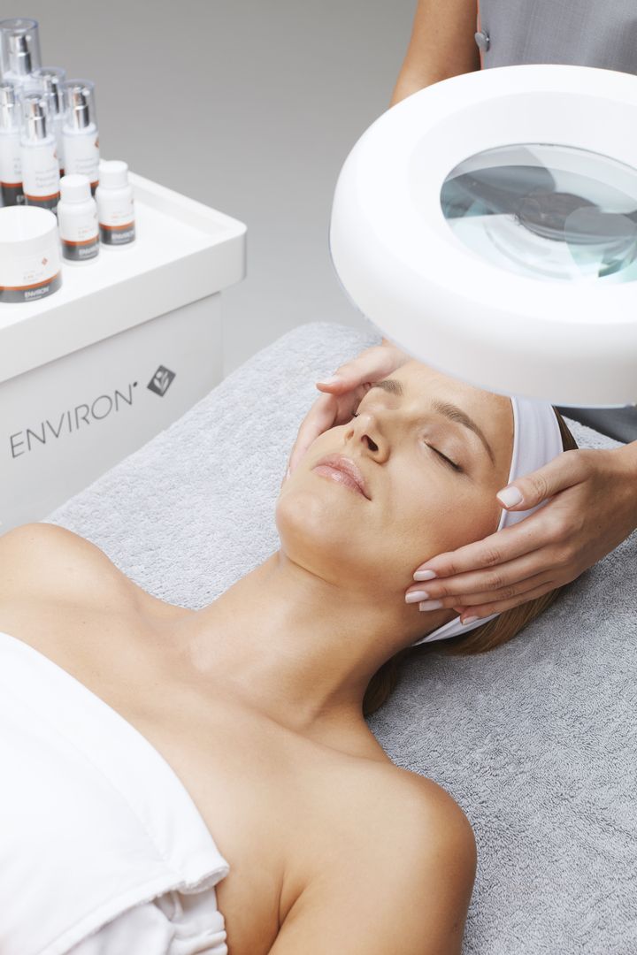 Eine Frau behandelt das Gesicht einer Frau unter einer Lupenleuchte.